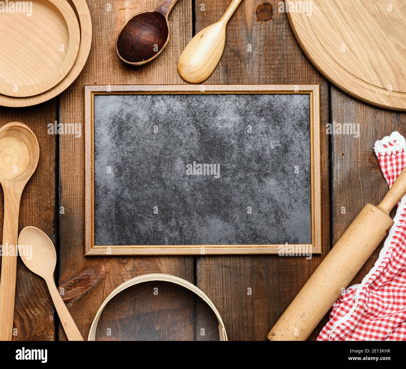 Leerer schwarzer Rahmen und Holzküche Vintage-Artikel: Sieb, Nudelholz, leere Löffel und runde Teller auf braunem Holztisch, Draufsicht Stockfoto