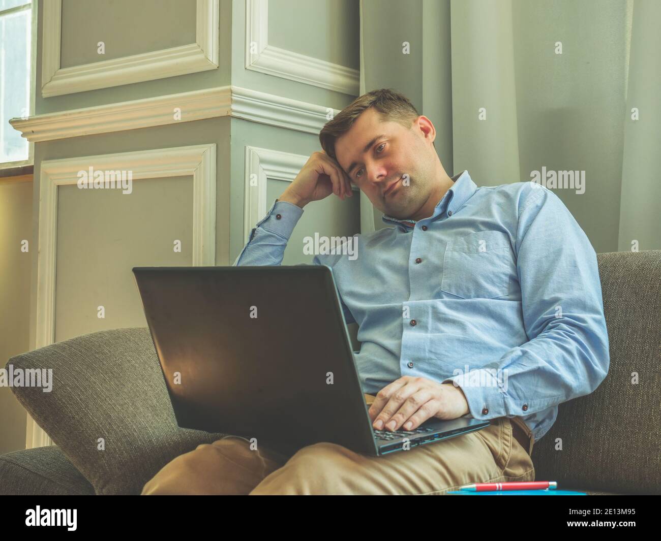 Müde trauriger Mann, der zu Hause auf der Couch mit einem Laptop sitzt. Stockfoto