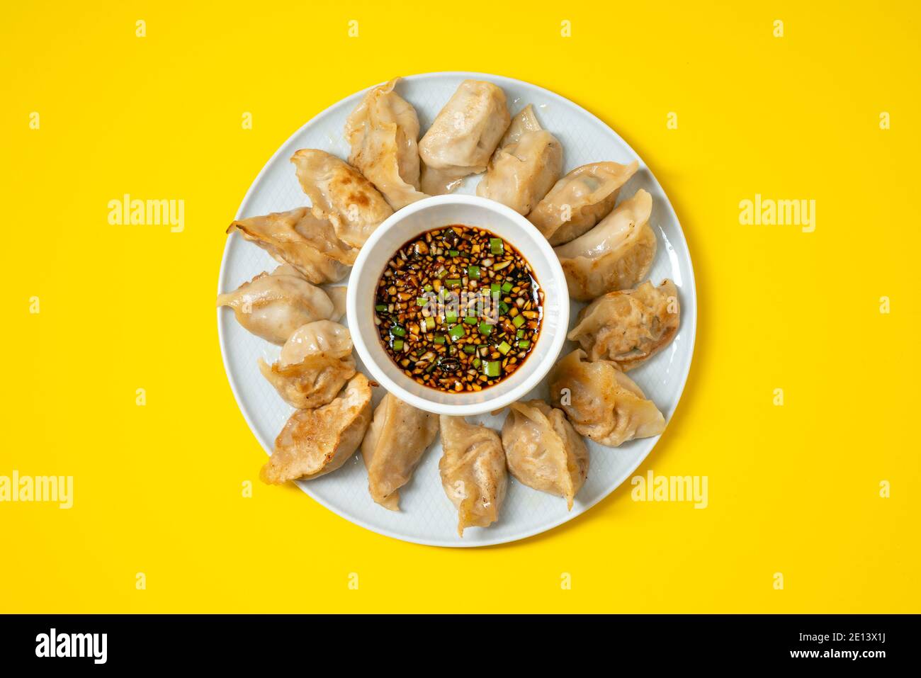 Gebratene Gyoza-Stil Knödel in einem Teller mit würziger Sojasauce auf gelbem Hintergrund. Asiatische Speisen zum Mitnehmen. Stockfoto