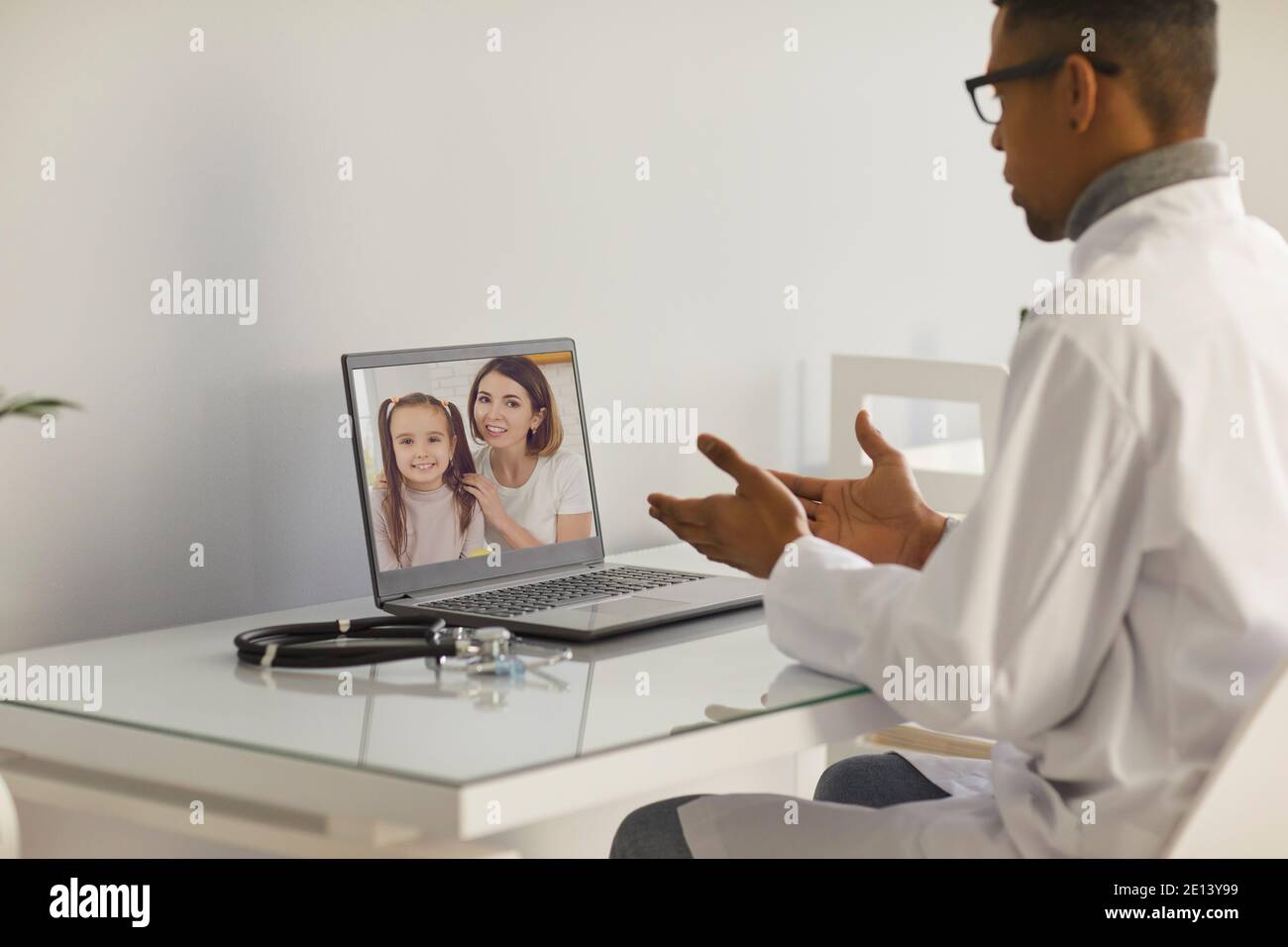 Hausarzt sitzt am Tisch mit Laptop und spricht mit Mutter und ihre Tochter Stockfoto