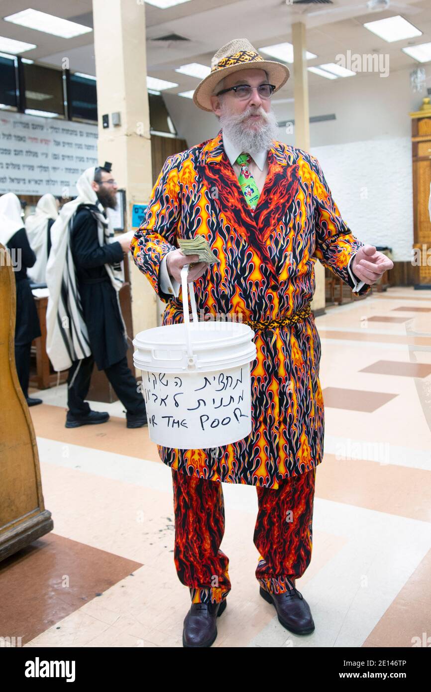 Ein chassidischer Rabbiner in einem sehr bunten Purim-Kostüm sammelt Nächstenliebe für die Armen. In einer Synagoge in Crown Heights, Brooklyn, New York, 2016. Stockfoto