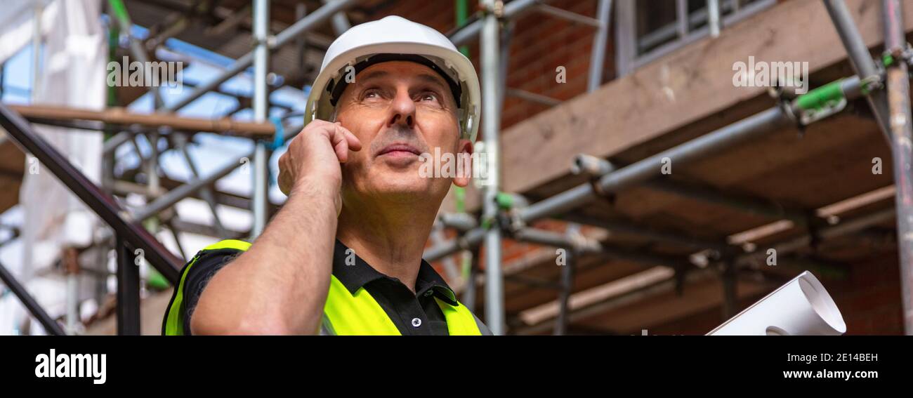 Panorama von männlichen Baumeister Vorarbeiter, Arbeiter oder Architekt auf der Baustelle hält Baupläne und sprechen auf seinem Handy Panorama-Web-Banner Stockfoto