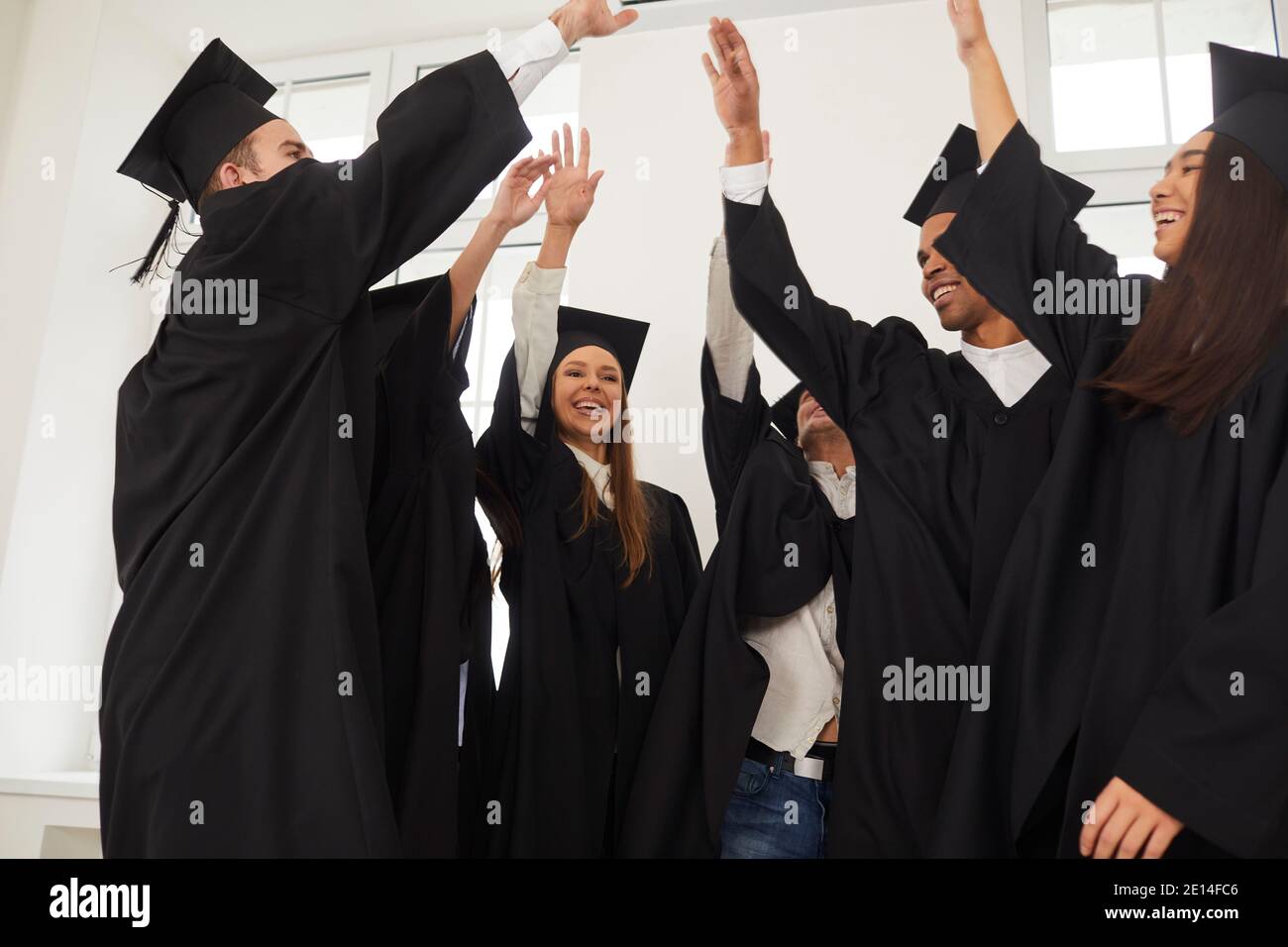 Absolventen heben die Hände, die sie übereinander gestapelt in einem Zeichen der Beendigung der Ausbildung. Stockfoto