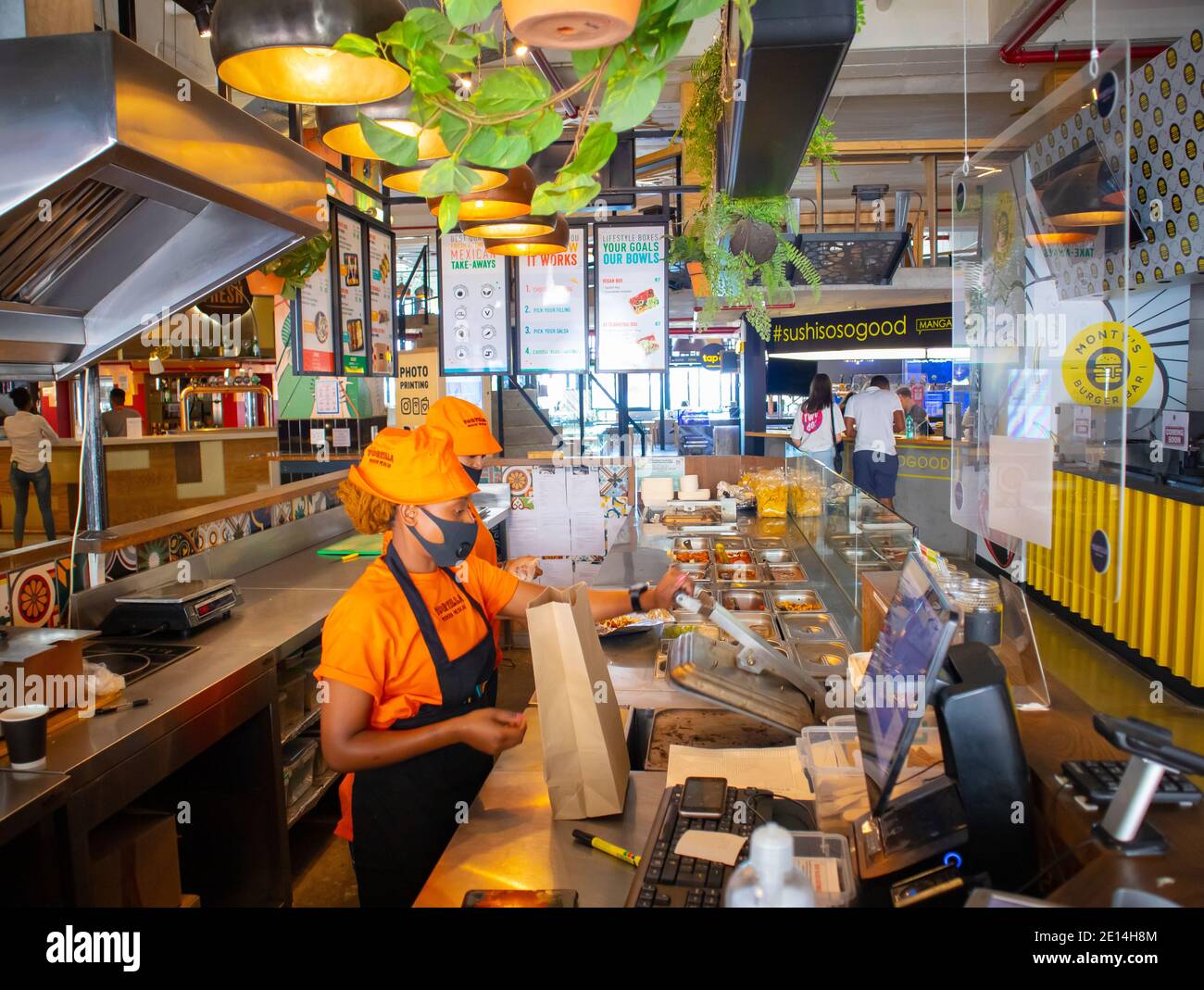 Mojo Markt- Kapstadt, Südafrika- 16/12/2020 Lebensmittelstand im Mojo Markt. Freundliches Personal mit leuchtend orangefarbenen Outfits und Gesichtsmasken, die Essen zubereiten Stockfoto