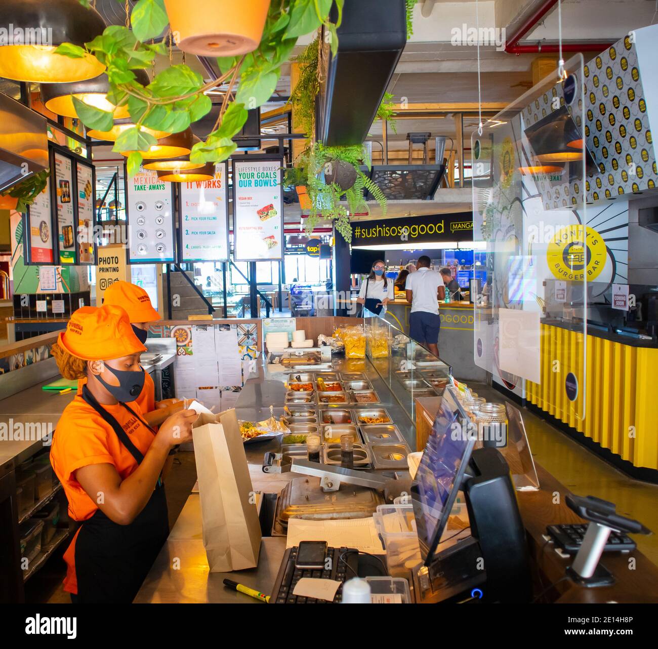 Mojo Markt- Kapstadt, Südafrika- 16/12/2020 Lebensmittelstand im Mojo Markt. Freundliches Personal mit leuchtend orangefarbenen Outfits und Gesichtsmasken, die Essen zubereiten Stockfoto