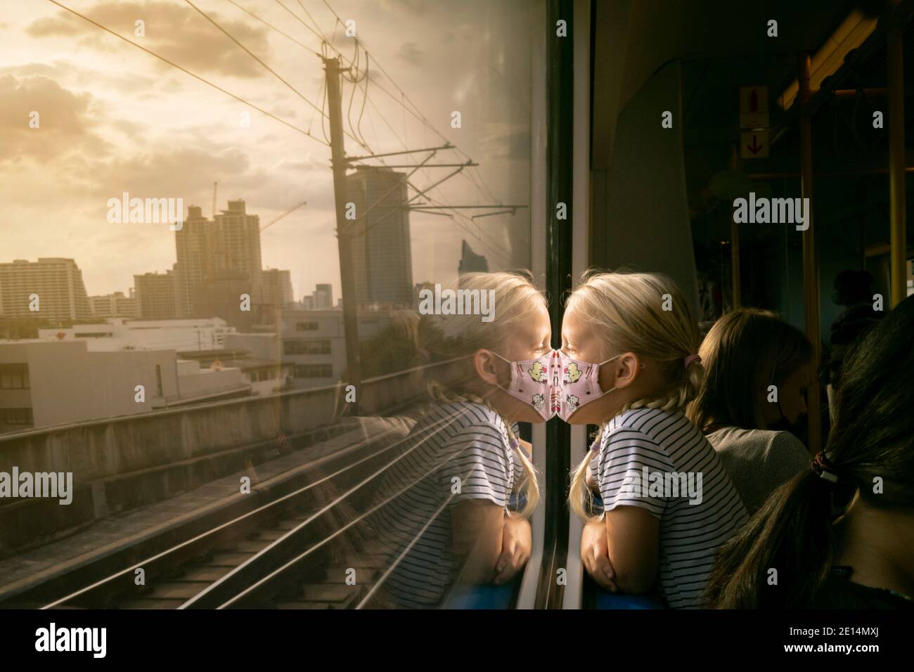 Bangkok, Thailand - 4. Januar 2021 : kleines Mädchen trägt Gesichtsmaske, um vor covid-19 oder Coronavirus Pandemie zu schützen, schaut aus dem Fenster auf c Stockfoto