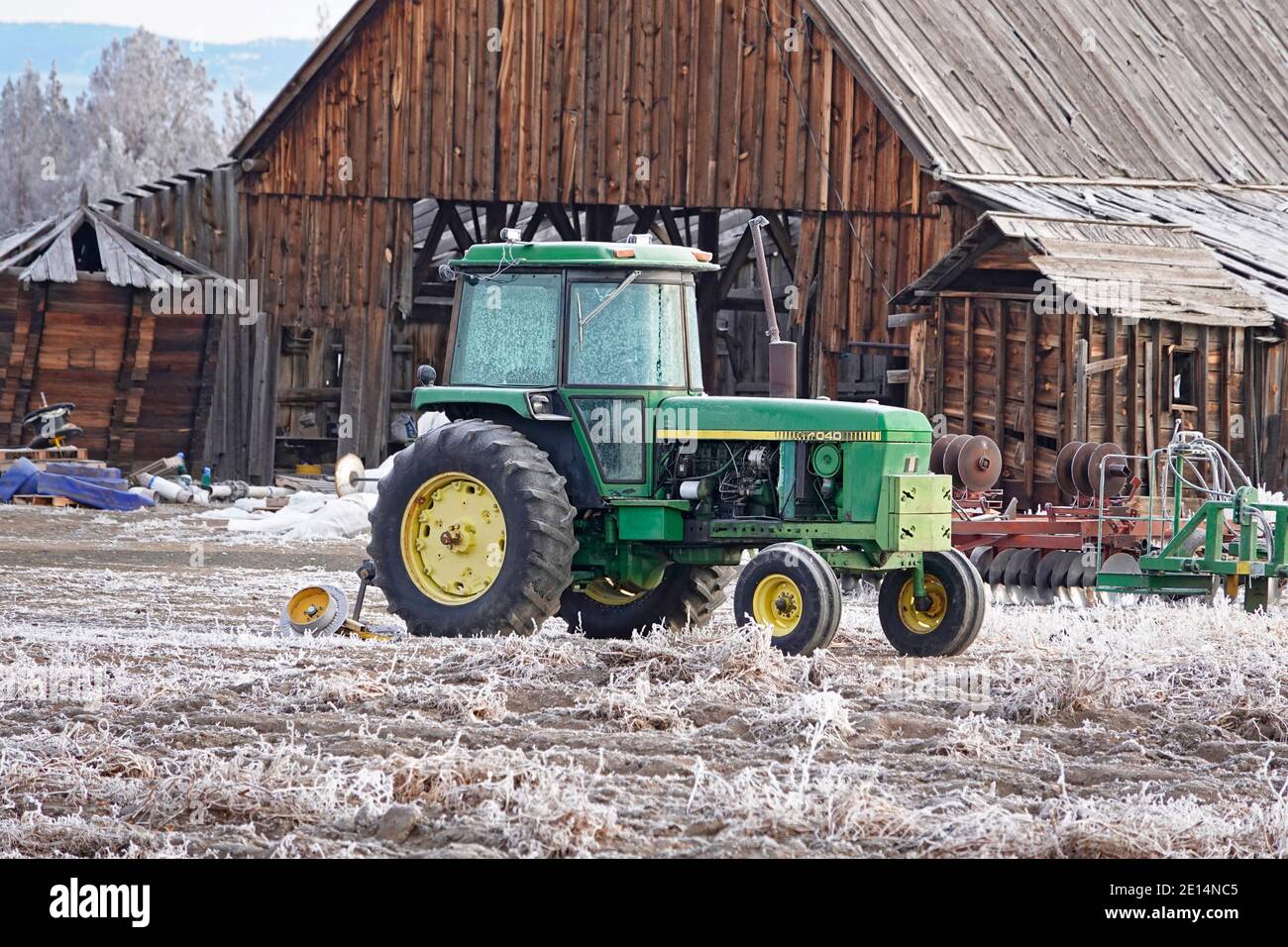 Ein Oldtimer-Traktor sitzt im Dezember vor einer noch älteren Holzscheune auf einer kleinen Farm in Tumalo, Oregon. Stockfoto