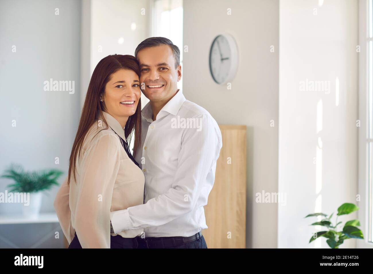 Glückliches Paar umarmt sich gegenseitig und schaut auf Kamera stehen Im Büro des Unternehmens Stockfoto