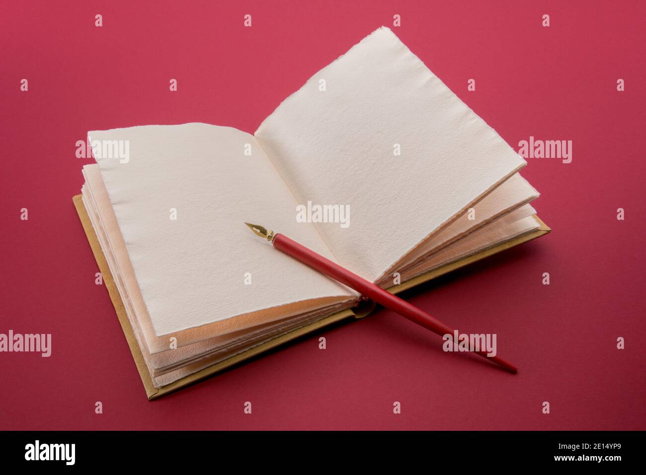Vintage roter Stift mit goldener Feder auf offenem antikem Leder hardcover-Notizbuch auf kardinalrotem Hintergrund Stockfoto