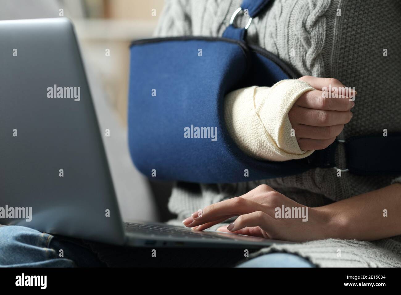 Nahaufnahme einer behinderten Frau Hände mit Laptop Ein gebrochener Arm in einer Schlinge auf einer Couch bei Zu Hause Stockfoto