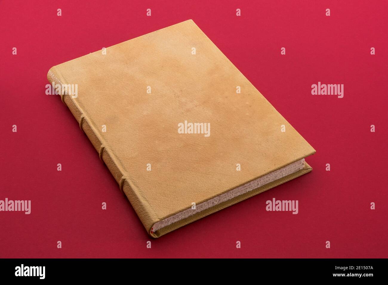 Antikes Buch mit hellbraunem Leder-Hardcover auf Kardinalrot Hintergrund Stockfoto