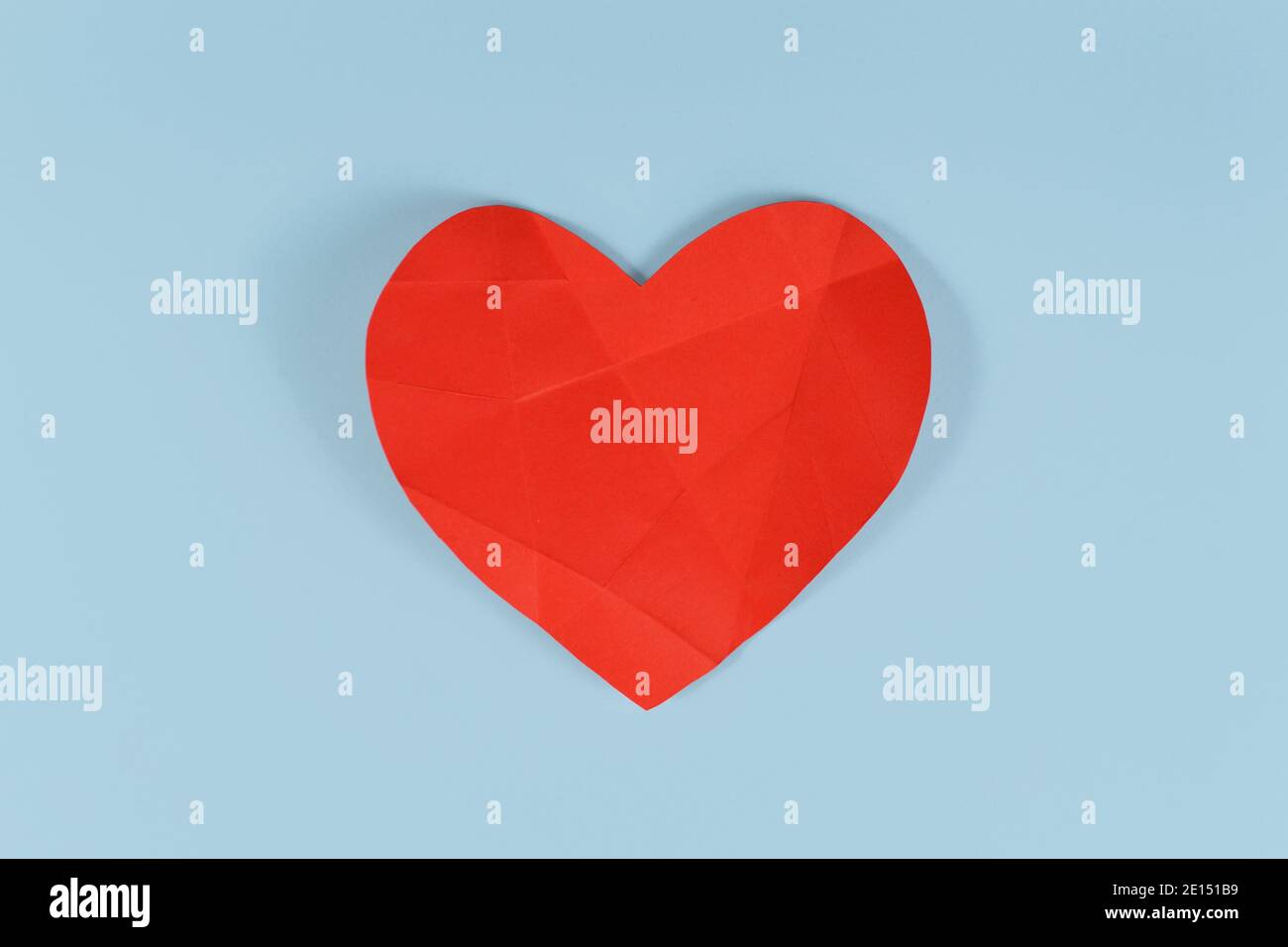 Gebrochenes rotes Papier Herz mit Falten Linien auf blauem Hintergrund. Konzept für gebrochenes oder krankes Herz Stockfoto