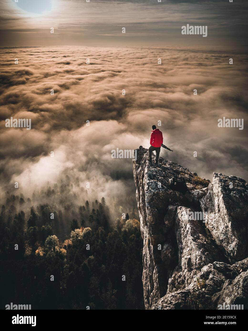Mann, der auf dem Berggipfel steht und den Sonnenuntergang über den Wolken beobachtet Stockfoto