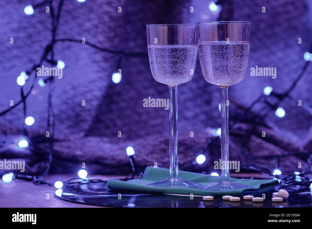 Selektives Fokusfoto von zwei Gläsern Champagner und Pillen auf dem Hintergrund einer Schallplatte, umgeben von heller Clubbeleuchtung Stockfoto