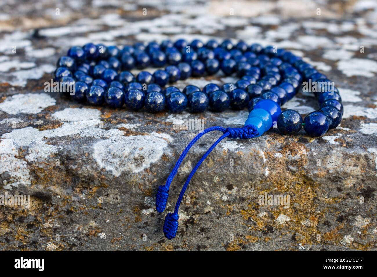 Blaue mala Perlen (Lapislazuli) an Steinwand, Nahaufnahme und selektiver Fokus. Achtsamkeit und Meditationszubehör. Stockfoto