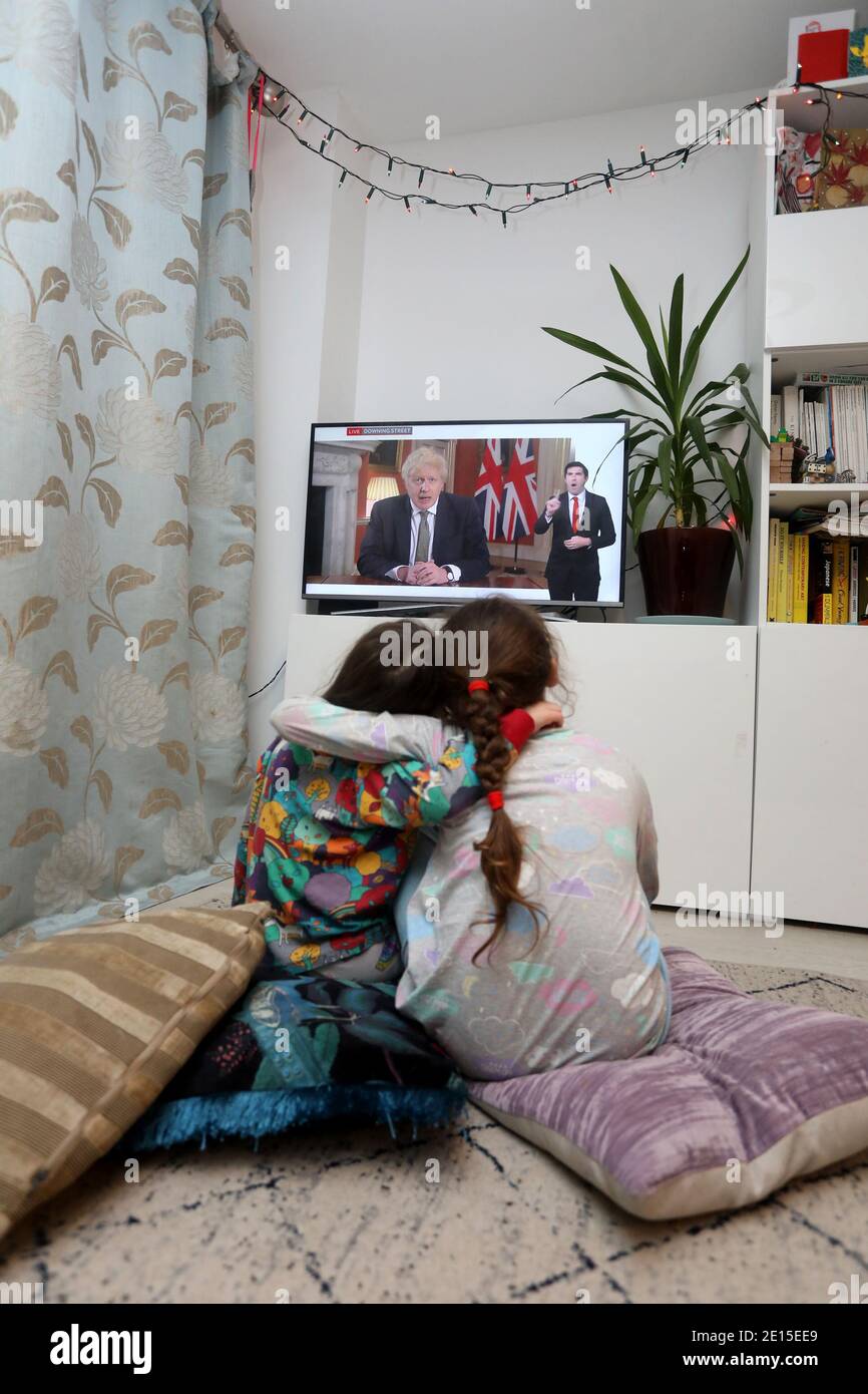 Chichester, West Sussex, Großbritannien. Florence, 5, (links) und ihre Schwester Isabelle, 8, (rechts) beobachten den britischen Premierminister Boris Johnson, der am Montag, den 4. Januar 2021 um 20 Uhr seine Rede hält und Großbritannien in seine dritte Absperrung bringt und seine Schulen schließt. Kredit: Sam Stephenson/Alamy Live Nachrichten Stockfoto