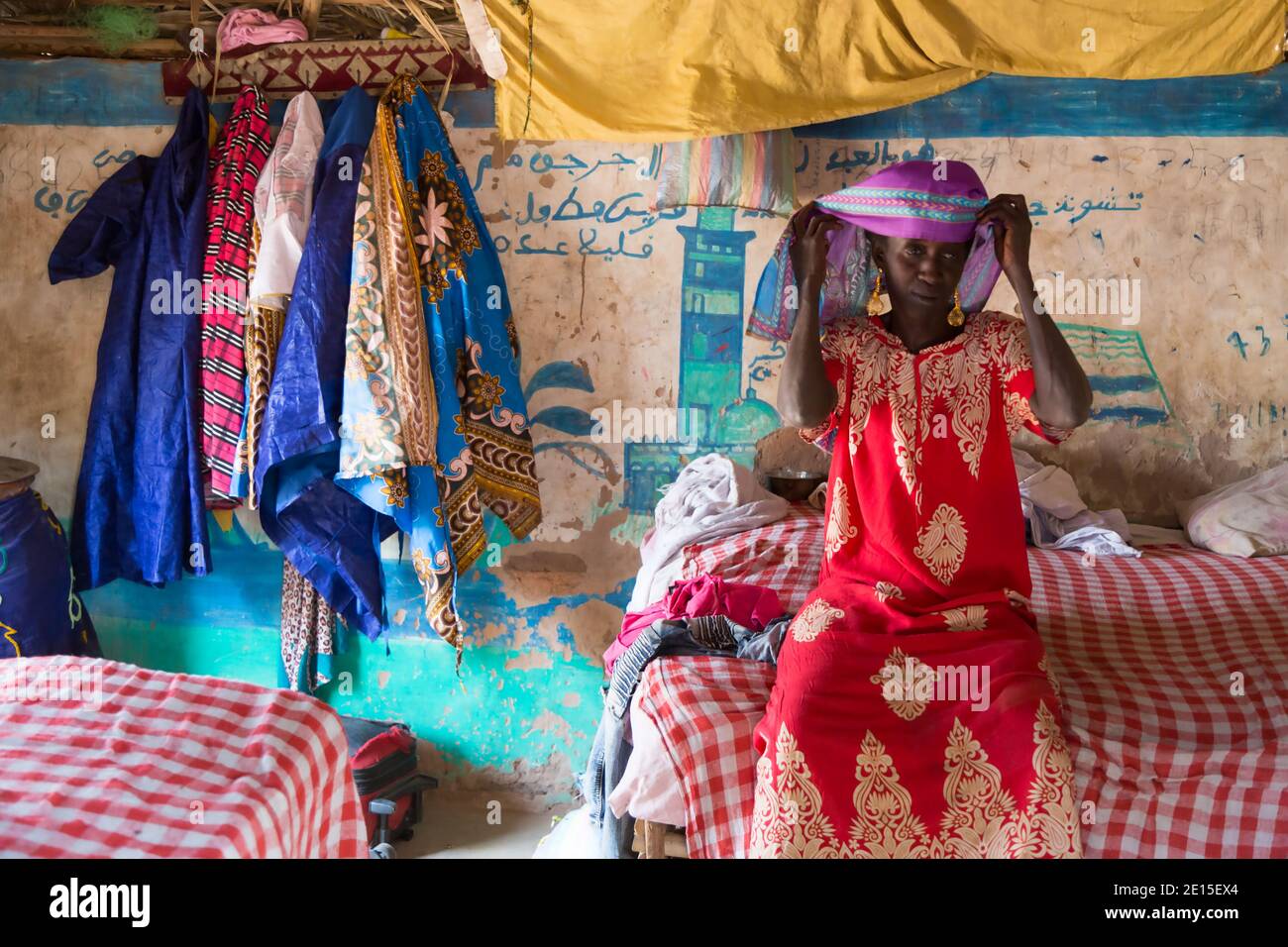 Eine gambische Dorfdame bindet ihre Kopfbedeckung, während sie auf ihrem Bett in einer traditionellen Schlammhütte in einem kleinen Weiler in der Nähe von Panchang, Gambia, sitzt Stockfoto