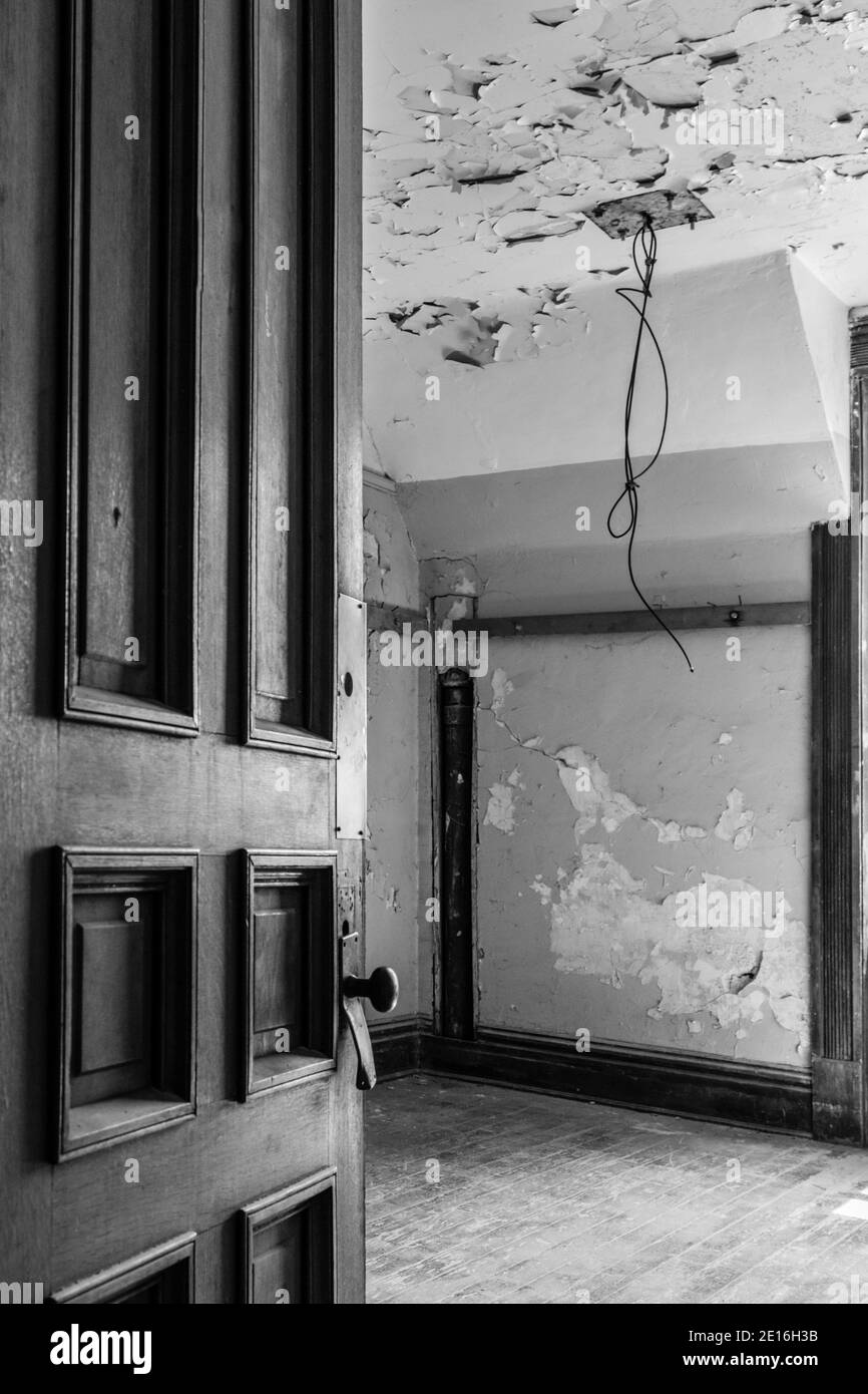 Die alte Holztür war teilweise offen und blickte auf einen verlassenen leeren Raum. Schwarz und Weiß in vertikaler Ausrichtung. Stockfoto