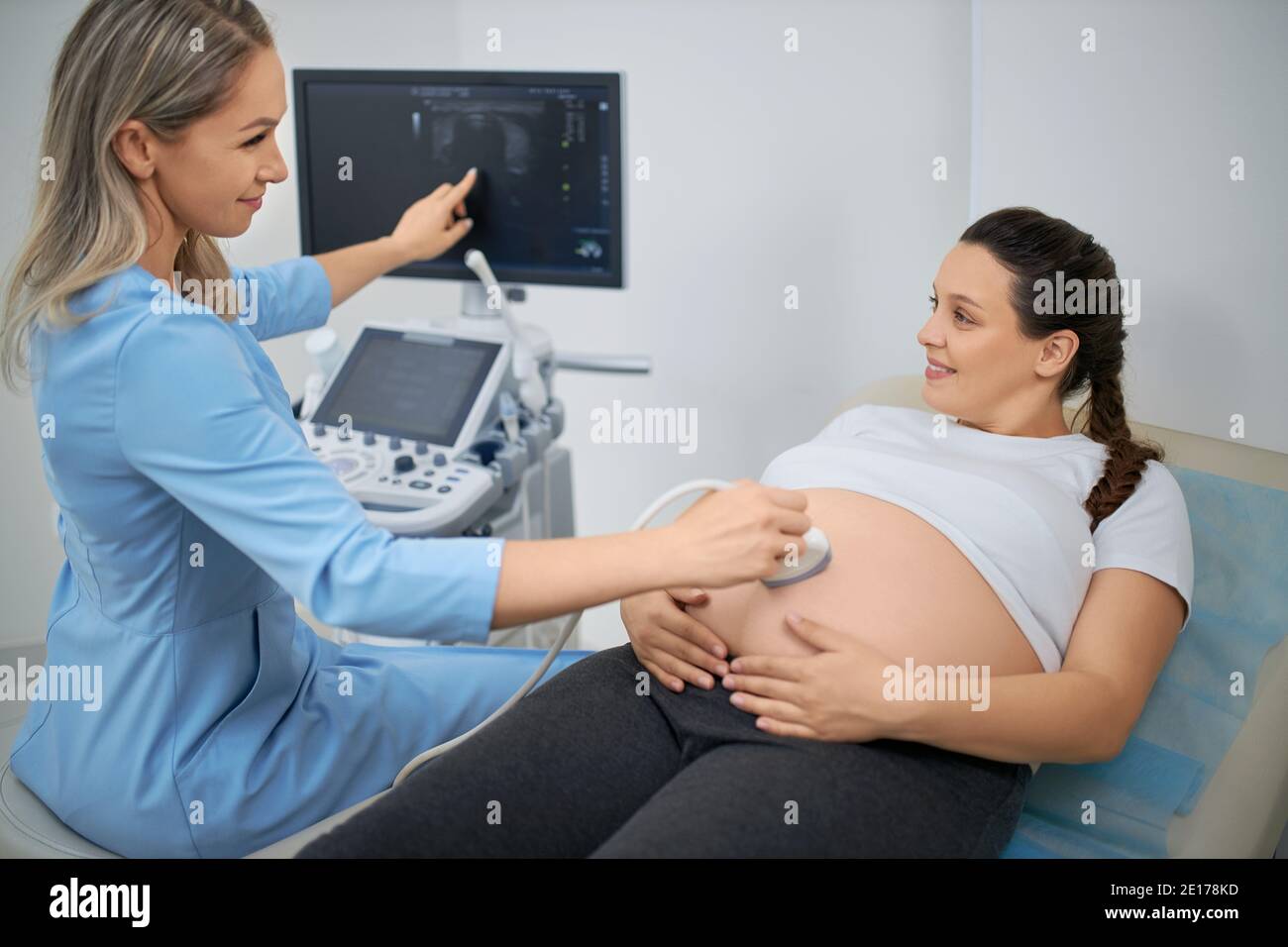 Glückliche Frau in Erwartung Besuch medizinische Klinik für Ultraschalluntersuchungen. Qualifizierter Arzt Untersuchung schwangere Klientin mit modernen medizinischen Geräten. Stockfoto