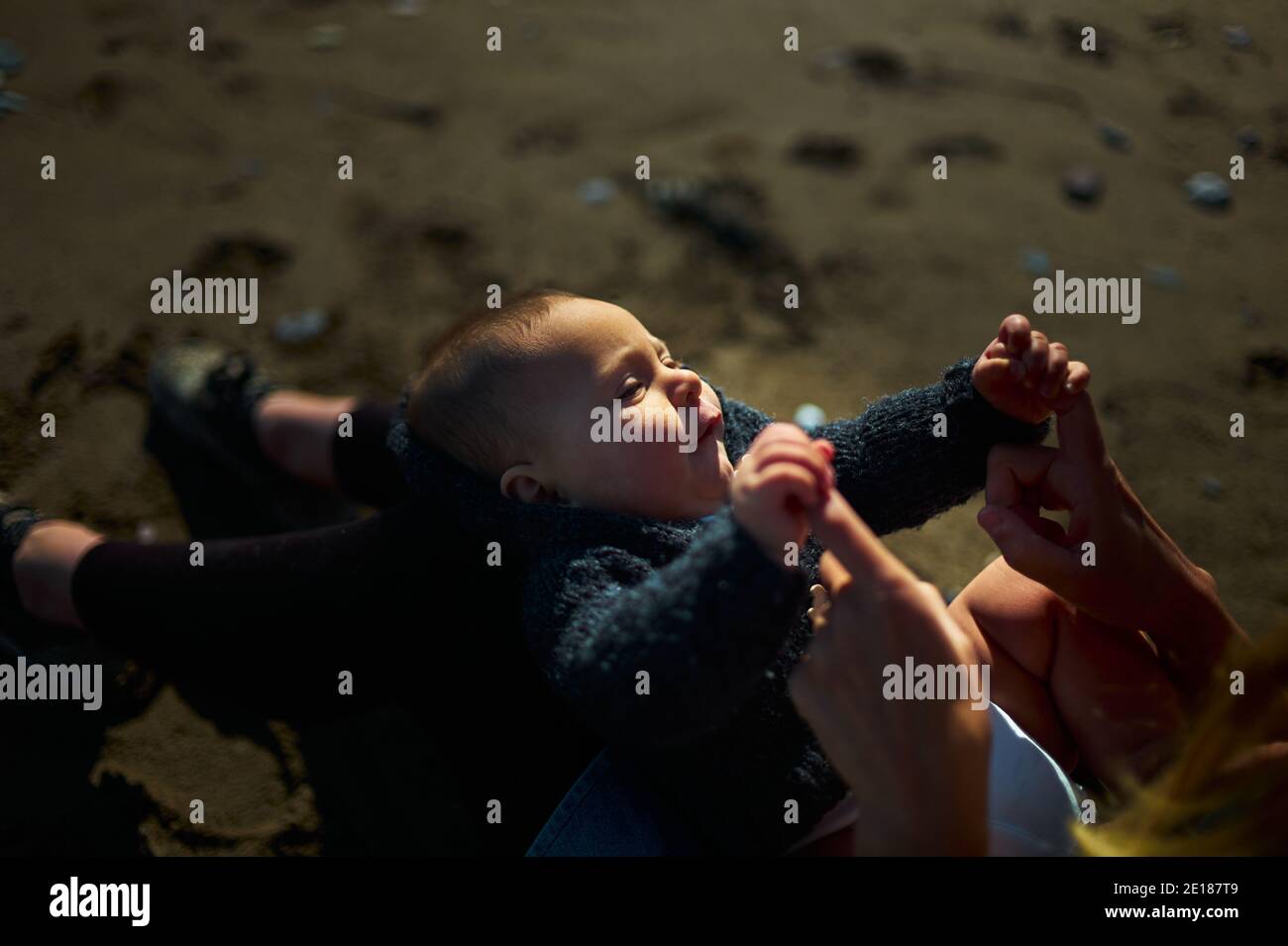 Ein kleines Baby ruht sich im Schoß seiner Mütter aus Der Strand an einem sonnigen Herbsttag Stockfoto