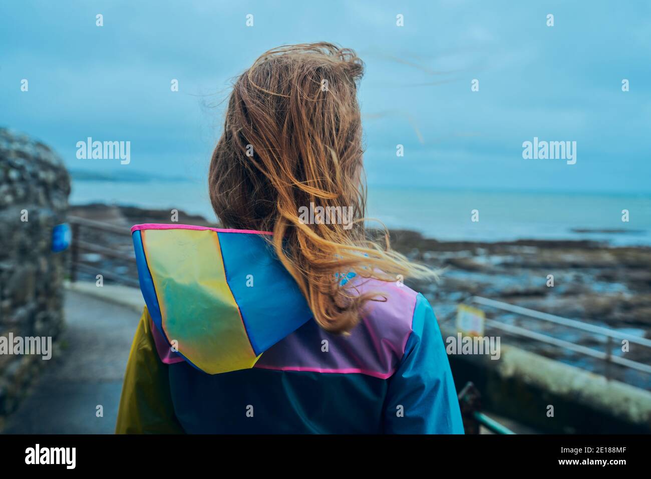 Eine junge Frau, die einen Regenmantel trägt, steht neben dem Am Meer Stockfoto