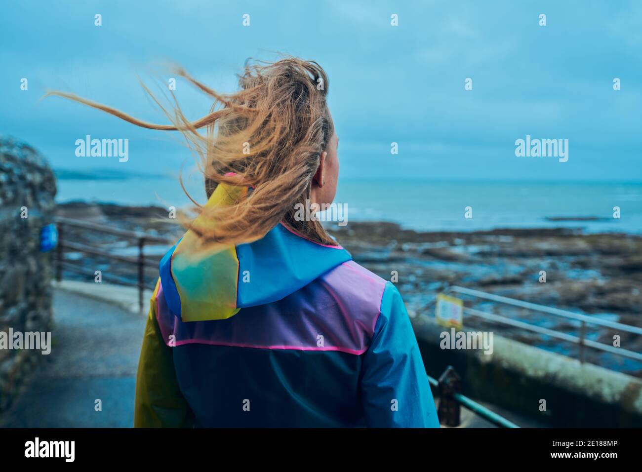 Eine junge Frau, die einen Regenmantel trägt, steht neben dem Am Meer Stockfoto