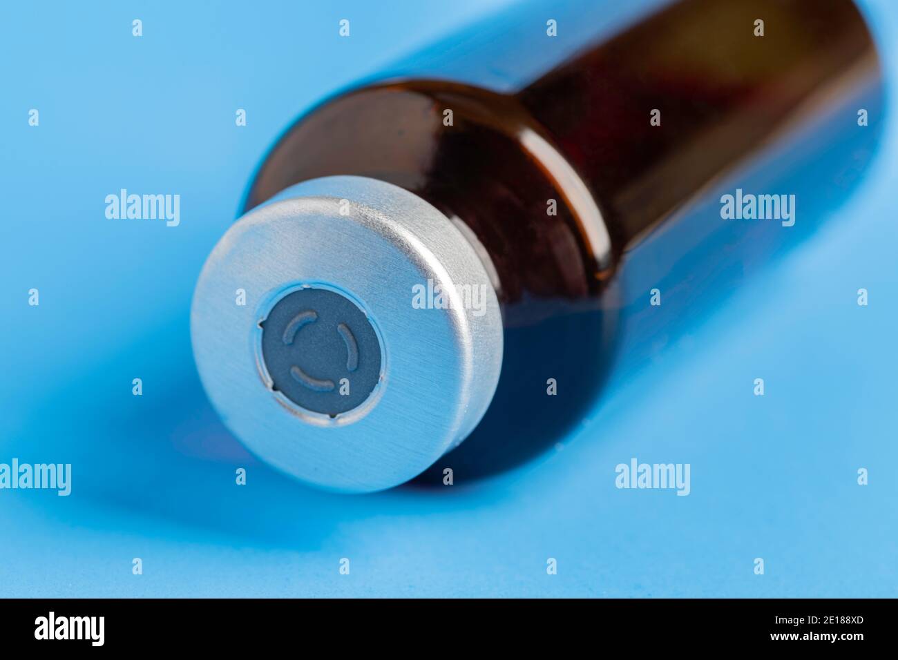 Eine Makroaufnahme mit selektivem Fokus auf einer bernsteinfarbenen Impfstoffflasche auf einem klaren blauen Hintergrund. Stockfoto