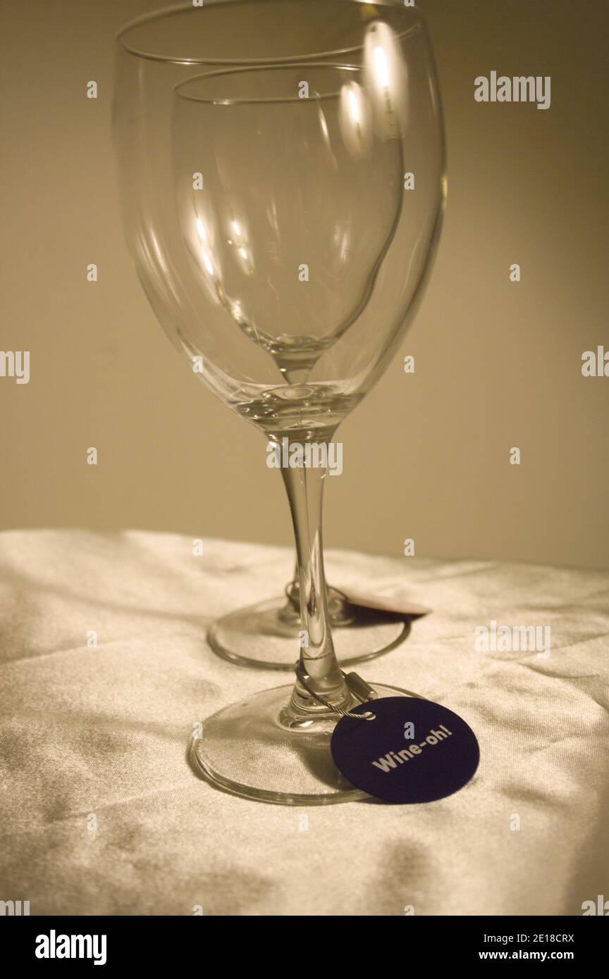 Zwei Weingläser sitzen auf einer seidigen, blassgoldenen Tischdecke. Jedes Glas hat einen Wein-Tag-Drink-Identifier auf der Basis. Stockfoto