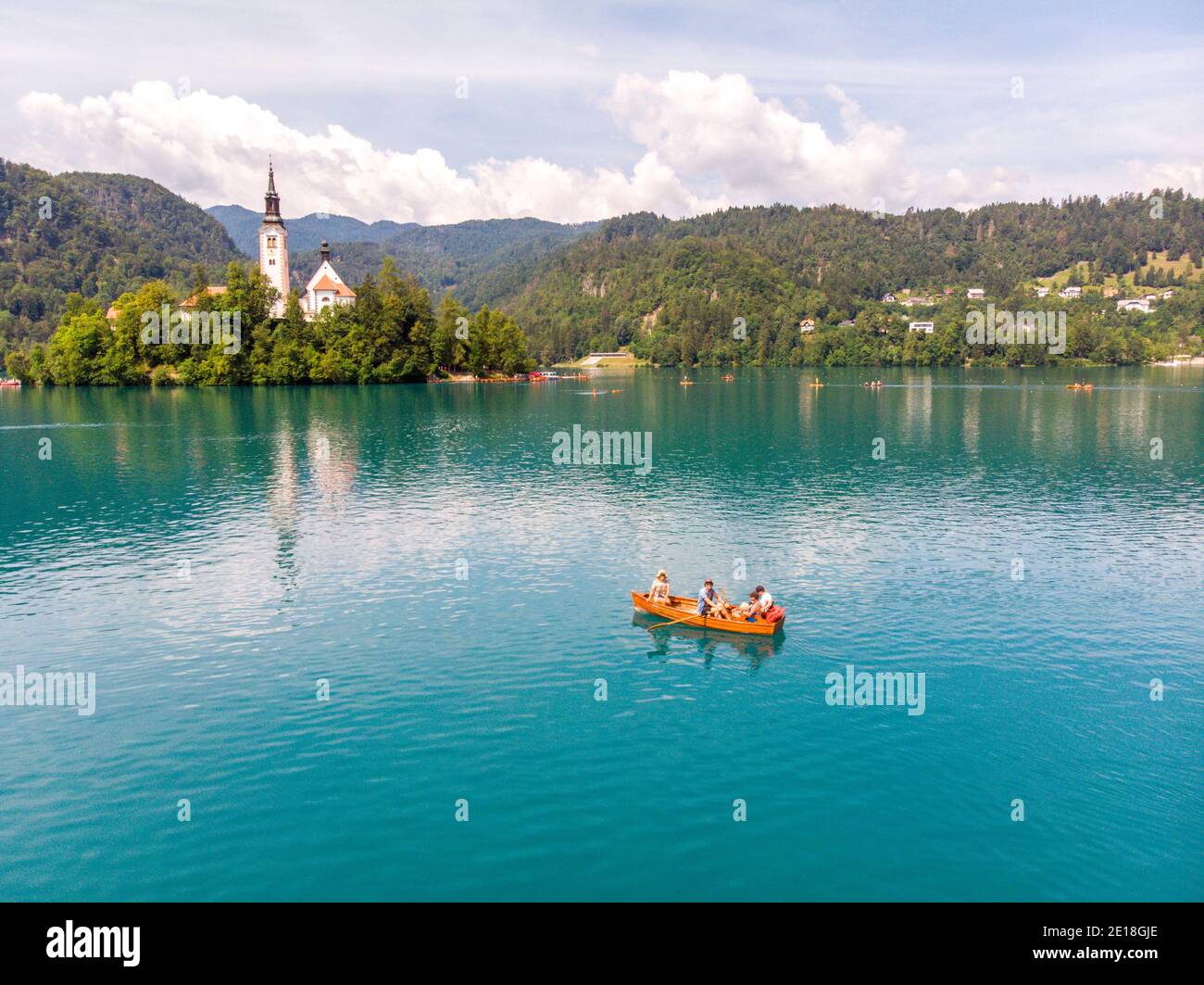 Drohnenbild der Familie rudern Traditionelles Holzboot auf dem See blutete mit der Kirche von Bled im Hintergrund Stockfoto