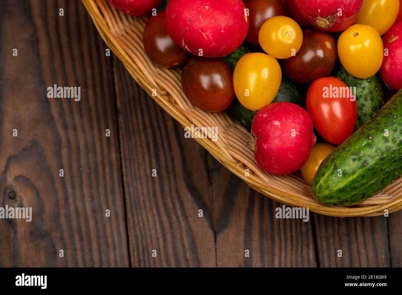 Grüne Gurken, reife Radieschen und bunte Tomaten in einem Weidenkorb Stockfoto