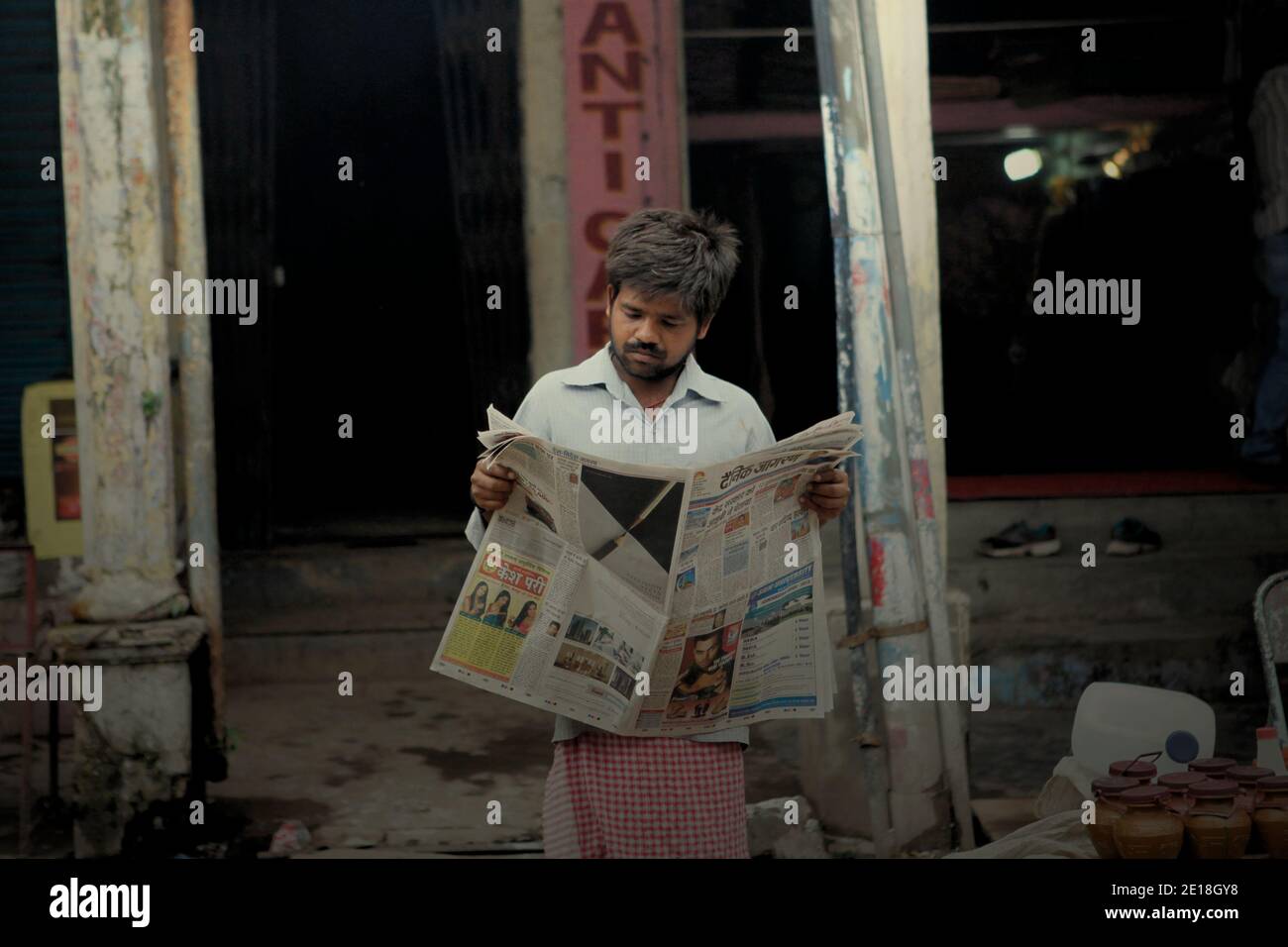 Ein Mann, der Zeitung am Straßenrand in Varanasi, Uttar Pradesh, Indien liest. Stockfoto