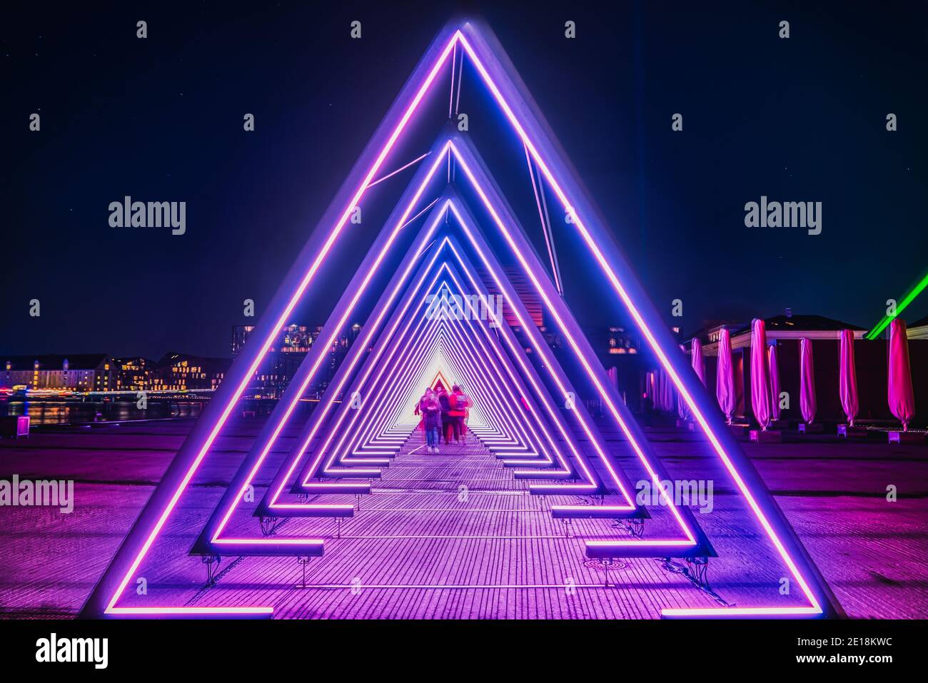 Lila gefärbte Tor Licht oder Licht Tunnel Installation aus dreieckigen Neon und LED-Leuchten. Verschwommene Menschen gehen durch den hellen tiefen Gang Stockfoto