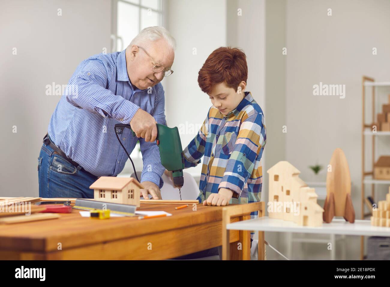 Großvater lehrt seinen Enkel mit Holz zu arbeiten und erklärt Wie man Bohrer verwendet Stockfoto