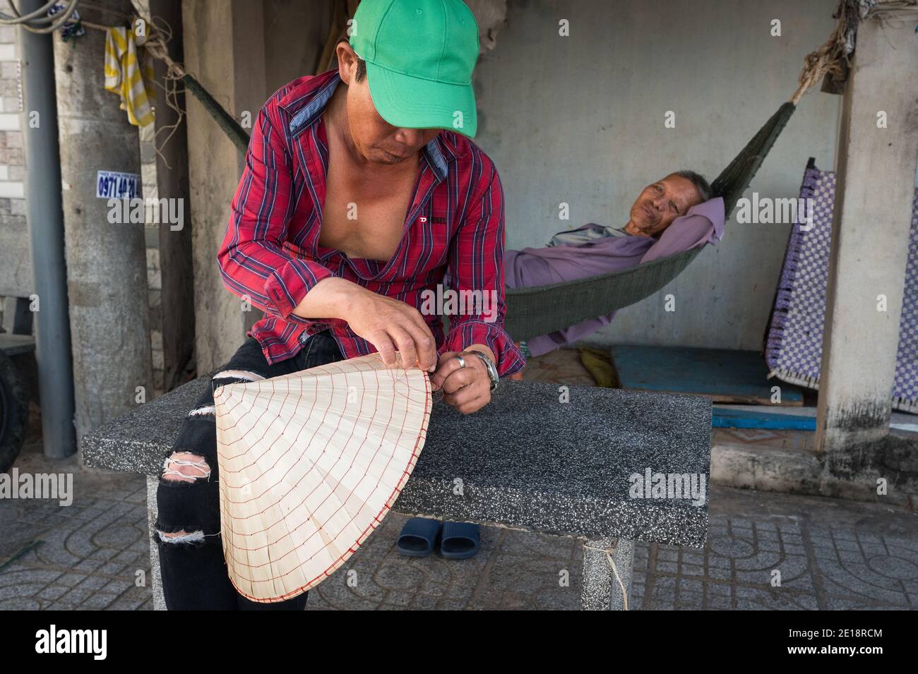 Mann, der auf einem konischen Hut vor seinem Haus, Phuoc Hai, Vietnam, arbeitet Stockfoto