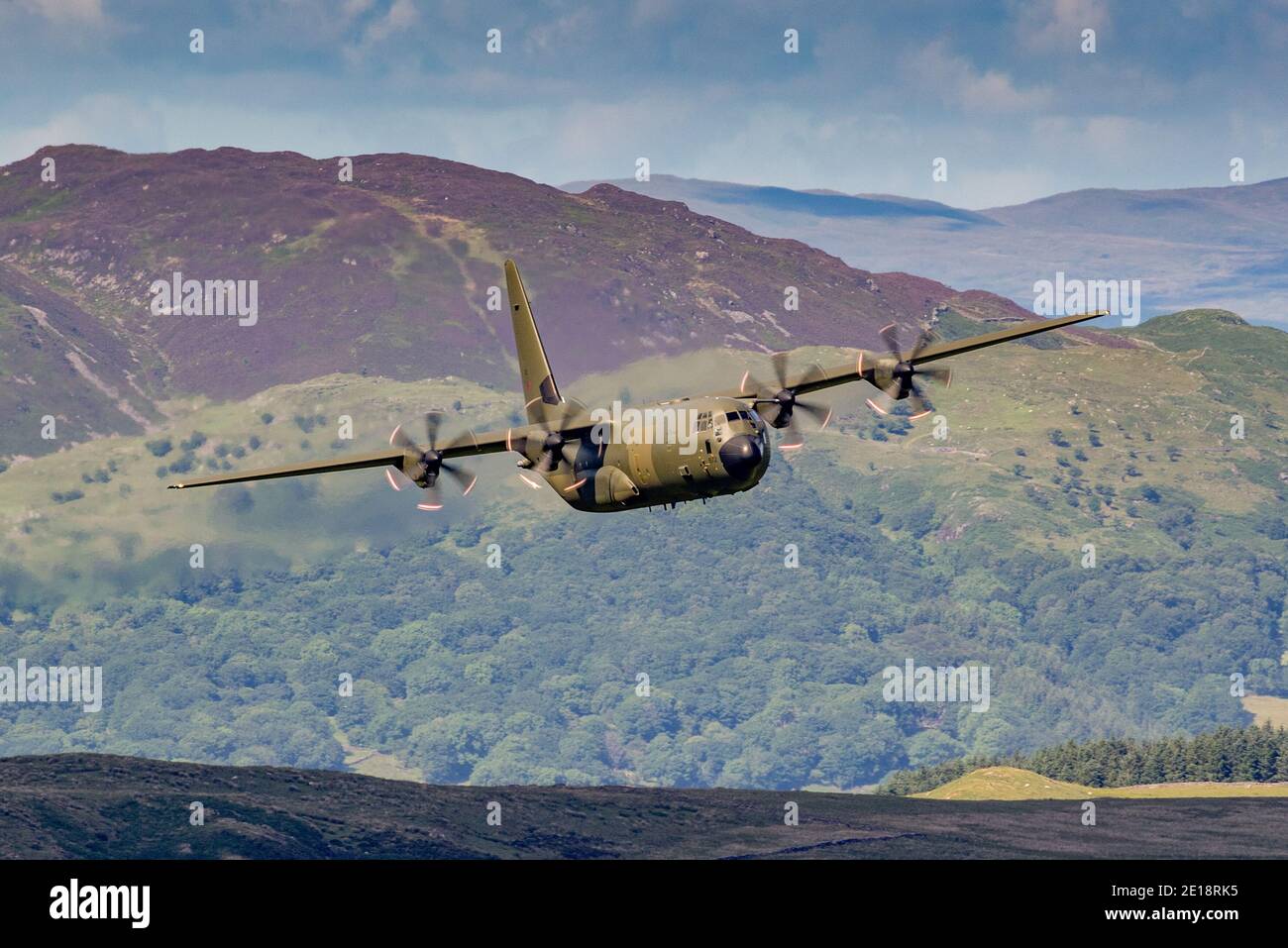 Lockheed C-130 Hercules fliegt tief in Tälern und Bergen. Grüne getarnte Truppe und Frachttransporter. Stockfoto