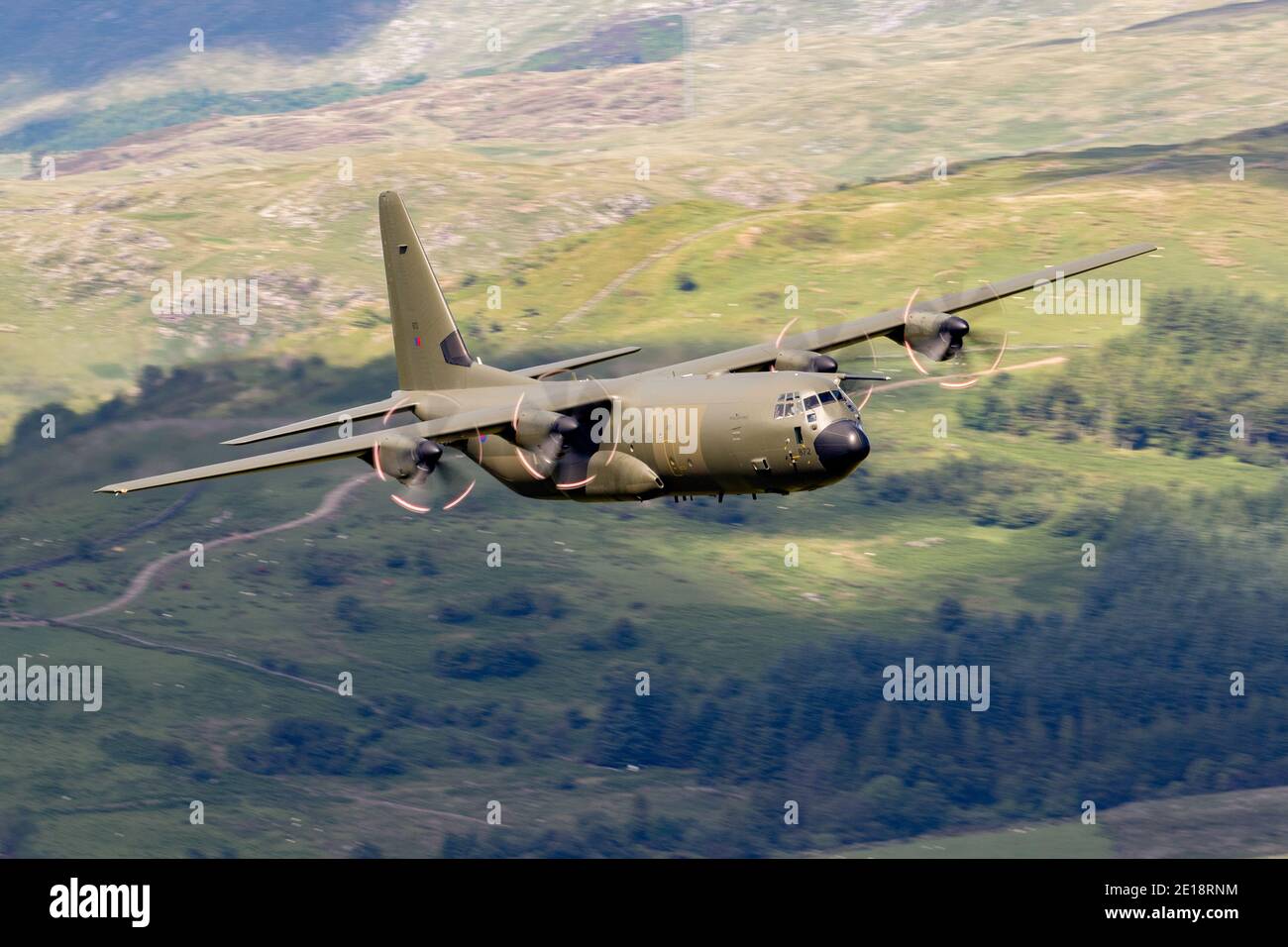 Lockheed C-130 Hercules fliegt tief in Tälern und Bergen. Grüne getarnte Truppe und Frachttransporter. Stockfoto