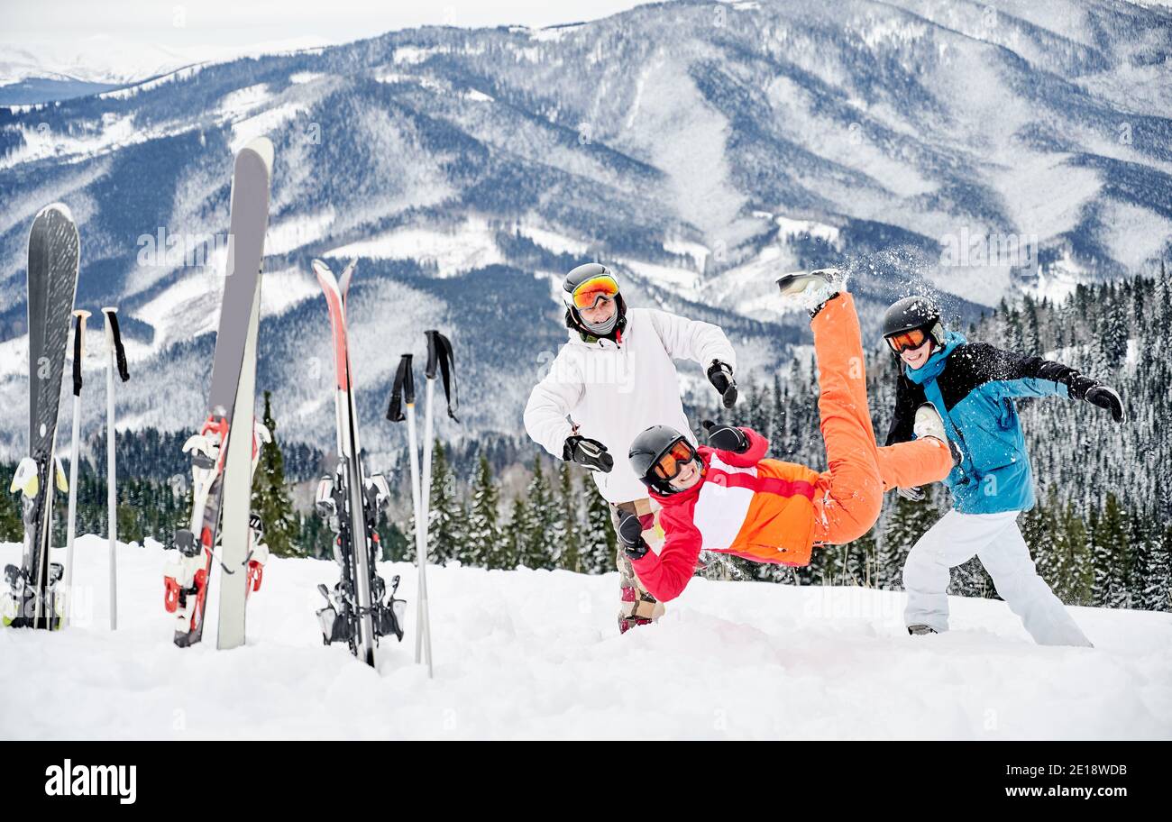 Gruppe von Freunden in lebhaften Wintersport-Anzügen Spaß im Schnee in den Bergen. Skistöcke und Skier stecken im Schnee, fröhliche Menschen spielen Schnee vor schönen Bergen Hintergrund. Stockfoto