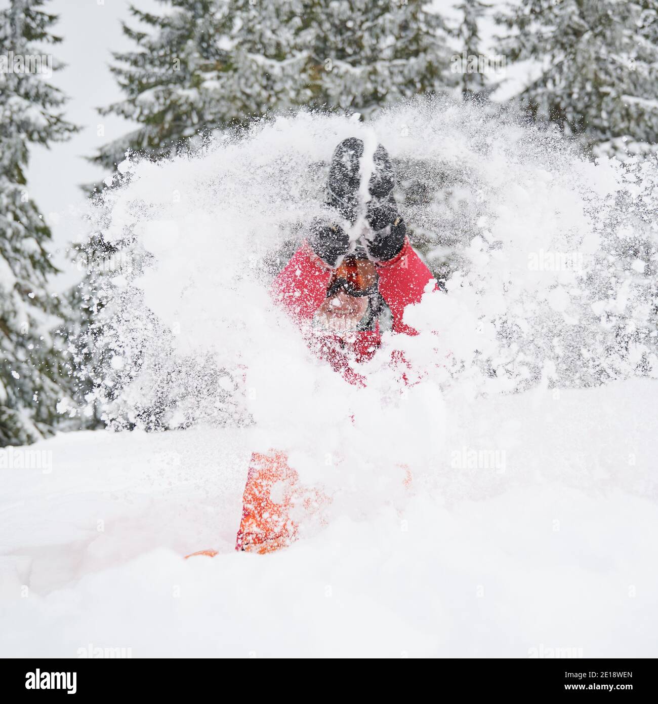 Glückliche Momente im Skigebiet in den Bergen. Frau im lebhaften Skianzug sitzen und spielen mit Schnee, werfen es auf. Konzept der Winterunterhaltung Stockfoto