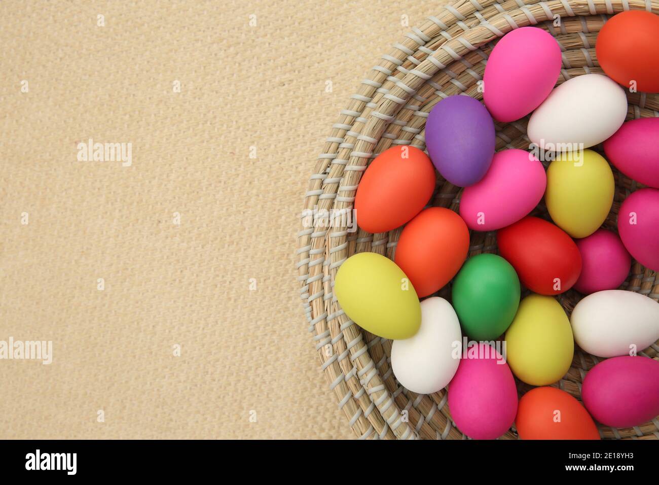 Bunte ostereier, in einem Strohkorb auf beigem Hintergrund. Stockfoto