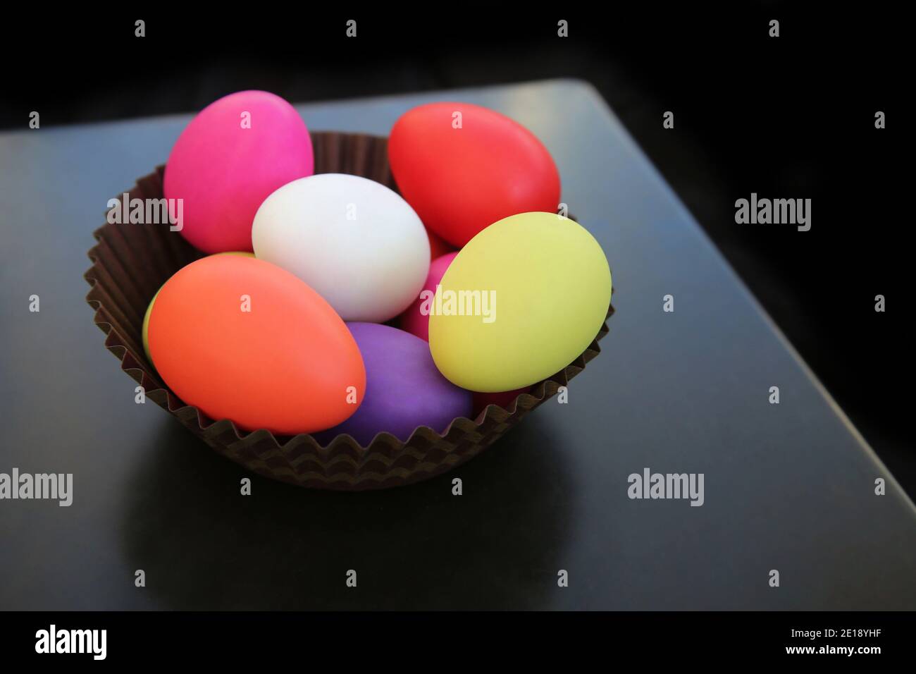 Bunt bemalte ostereier in rot, rosa, gelb, grün und weiß in einem braunen Papierkorb vor dunklem Hintergrund. Stockfoto