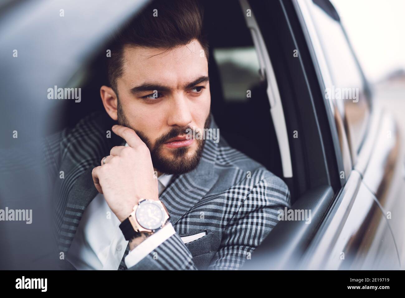 Schöner bärtiger Geschäftsmann in einem Anzug, der vor einem Fenster eines teuren Autos schaut. Stockfoto
