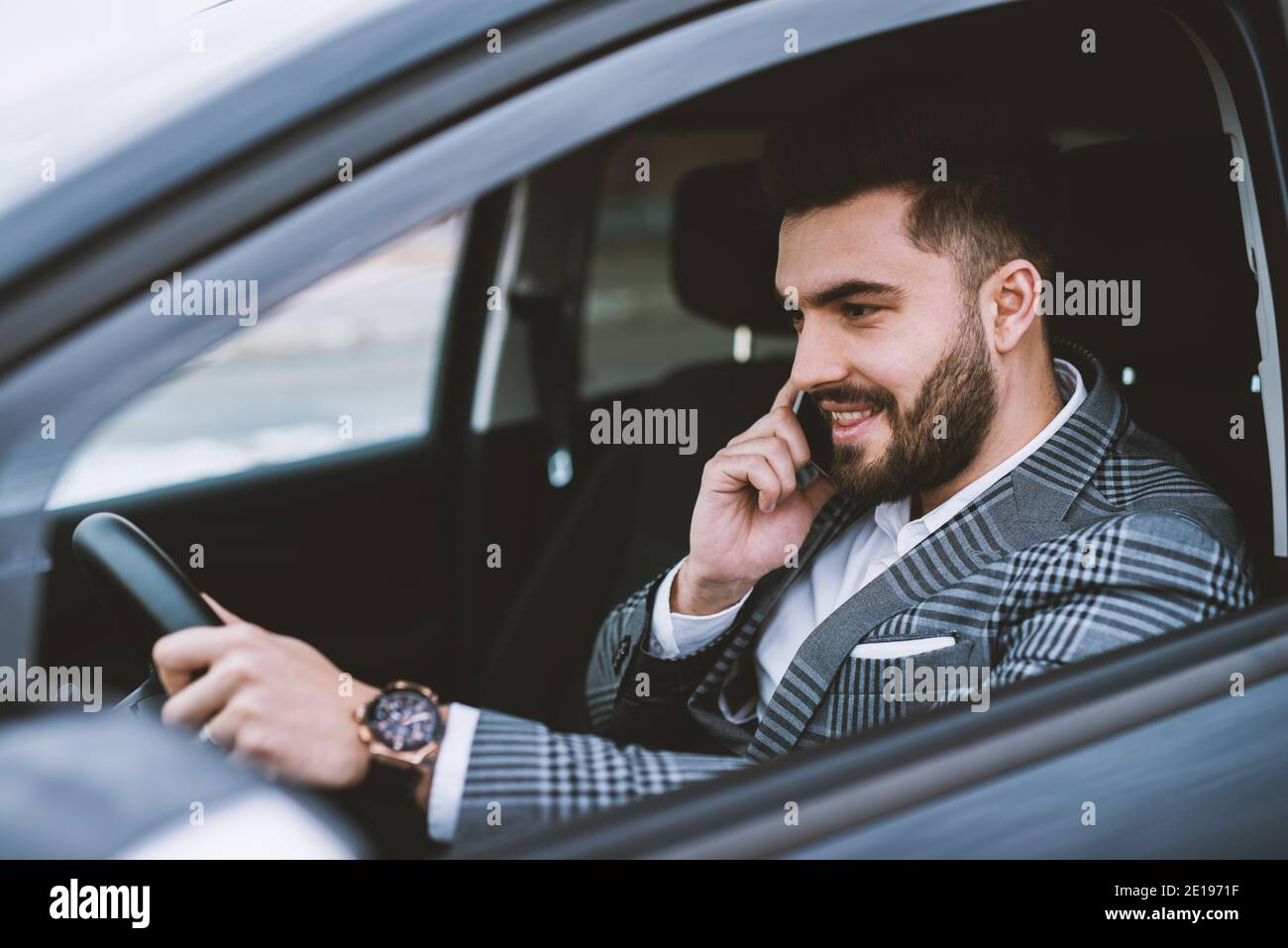Attraktiver Mann in einem Anzug, der einen Anruf beim Autofahren in einer Stadt macht. Stockfoto
