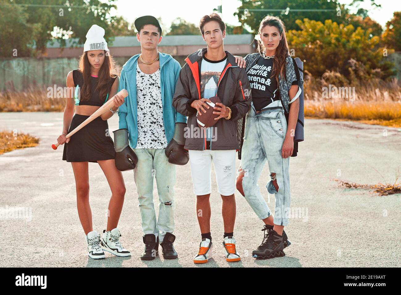 Portrait einer interracial Gruppe von 4 jungen Erwachsenen, die zusammen auf einem alten Parkplatz vor einem alten Graffiti-besprühten Ladenfront stehen. Stockfoto