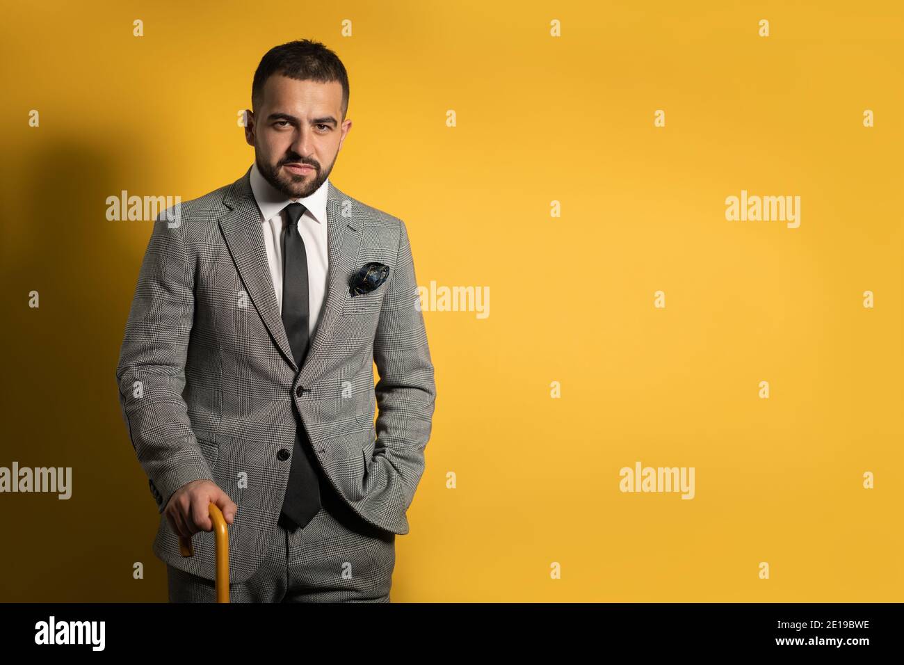 Old School trendy stilvolle schöne junge Mann trägt grauen Anzug Mit einer Hand angehoben stehend mit Stock oder Schirm in Seine Hand isoliert auf gelb Stockfoto