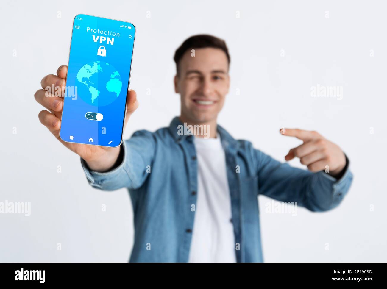 Lächelnder Kerl hält und zeigt Smartphone mit vpn-App Stockfoto