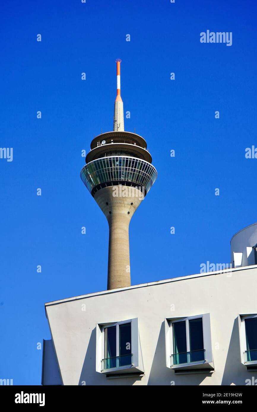 Der Rheinturm, Düsseldorfs Wahrzeichen, mit einem Teil eines weißen Gebäudes, das vom Stararchitekten Frank O. Gehry im Neuen Zollhof, Medienhafen, entworfen wurde. Stockfoto