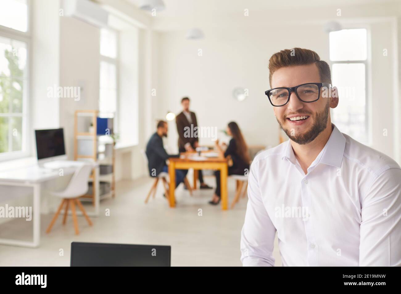 Lächelnder Büromitarbeiter, der die Kamera anschaut, und Kollegen, die ein Brainstorming durchführen Im Hintergrund Stockfoto