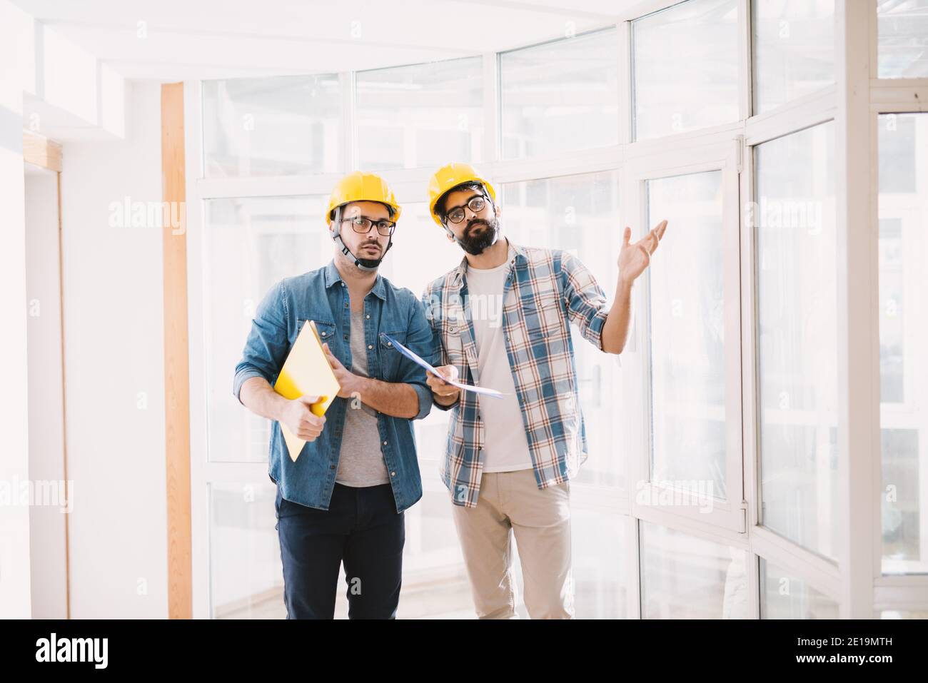 Zwei fokussierte junge professionelle Ingenieure mit Helmen suchen, wie ein Problem bei der Projektplanung zu lösen. Stockfoto