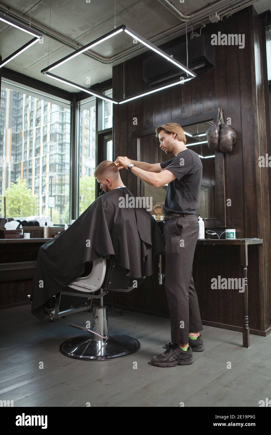 Volle Länge vertikale Aufnahme eines Barbiers in seinem Salon arbeiten, schneiden Haare von männlichen Kunden Stockfoto