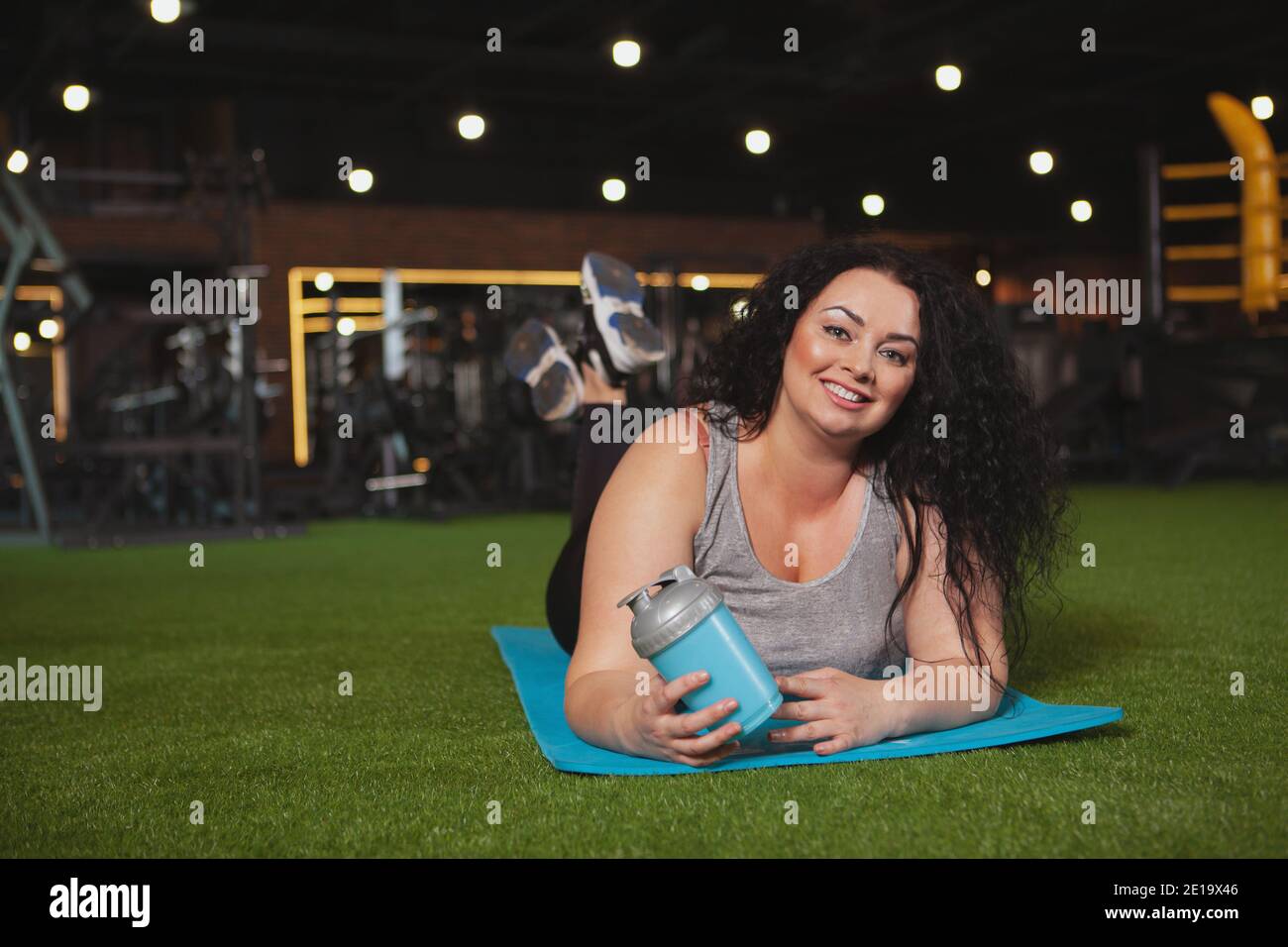 Fröhliche Plus Größe Frau entspannen im Fitnessstudio nach dem Training, liegend auf Yoga-Matte, kopieren Raum. Glücklich schöne übergewichtige Sportlerin, die beim Sport ruht Stockfoto